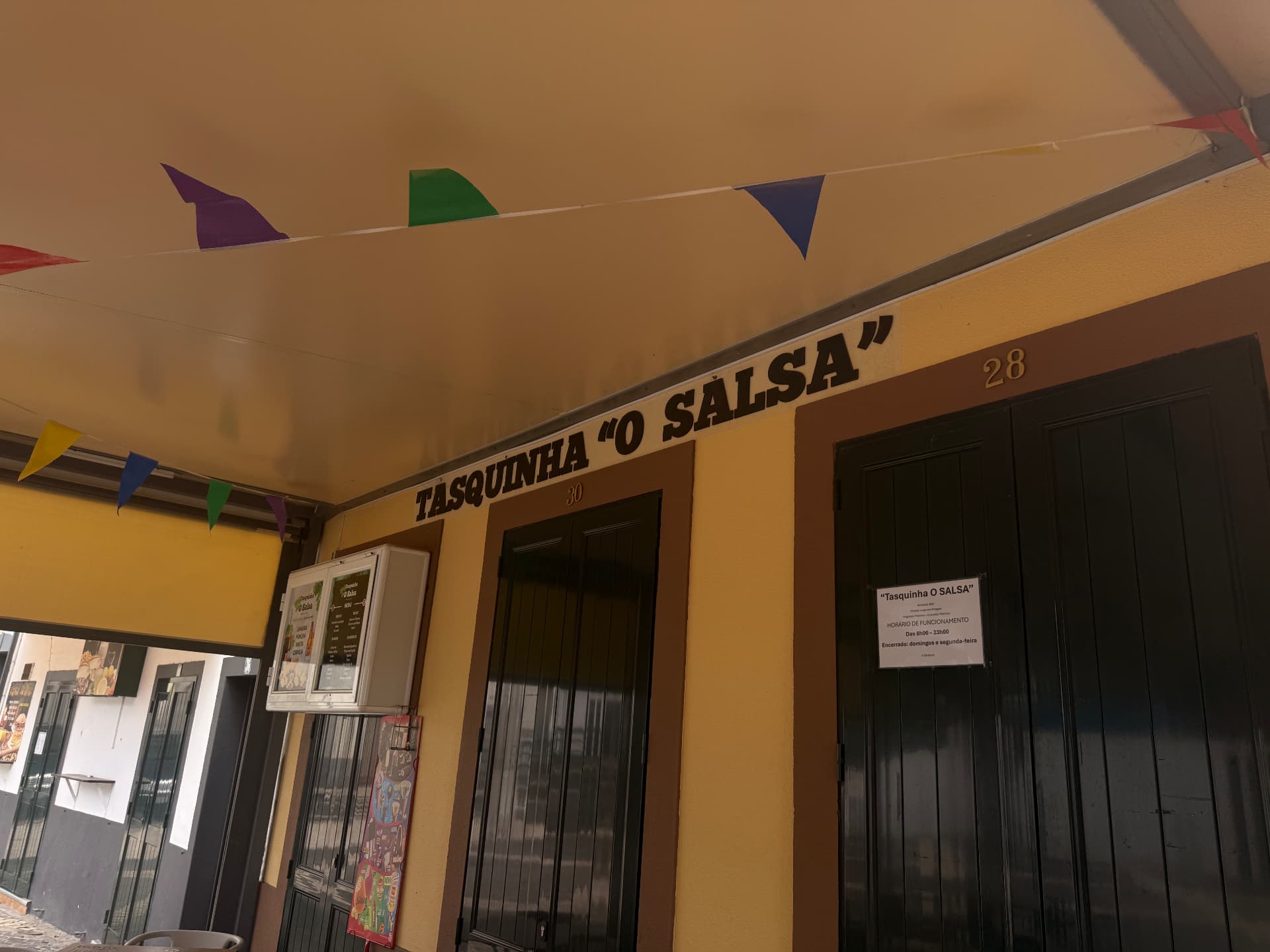 Tasquinha O Salsa sign under the awning with festival bunting, Machico